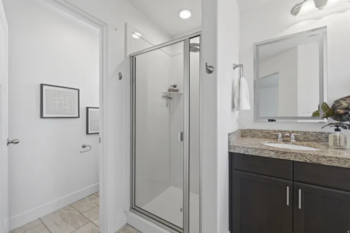 Shower enclosure with clear glass door, dark wood-finish vanity with a light-toned countertop, integrated sink, and a framed mirror