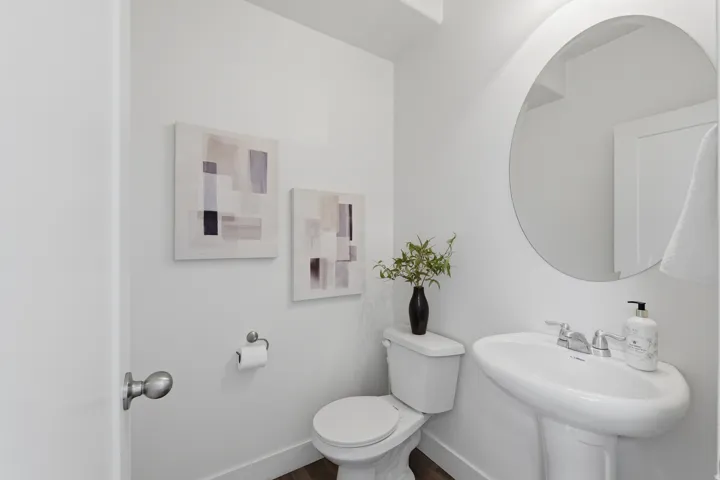 Pedestal sink with chrome fixtures, round wall mirror, and wood-finish flooring
