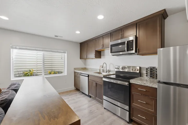 Kitchen featuring stainless steel appliances, wood-finish cabinetry, stone countertops, and wood-finish flooring