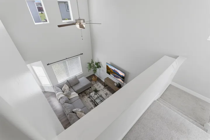 Two-story living area with high ceilings, wood-finish flooring, and a ceiling fan
