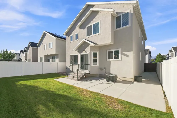 Expansive lawn area, concrete patio, white privacy fencing, exterior stucco finish, and a rear deck with steps