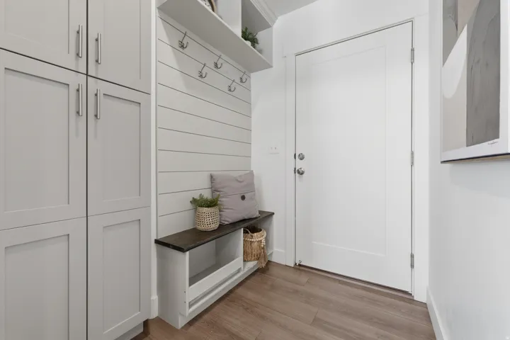 Built-in cabinetry with ample storage, wood-finish flooring, white shiplap wall accent, integrated bench with a dark wood top, and wall-mounted coat hooks