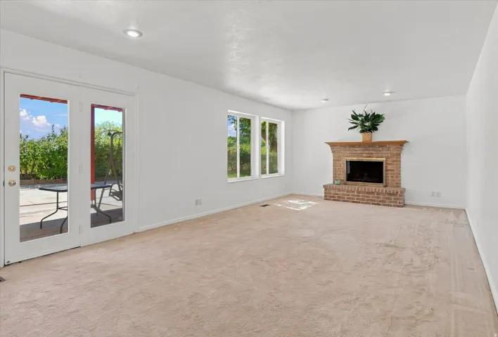 Brick fireplace with a wood mantle, double glass-paneled doors, recessed lighting, and multiple windows