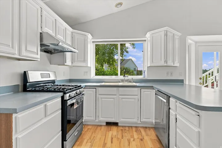 Kitchen featuring white cabinetry, light-toned countertops, a stainless steel gas range, and wood-finish flooring