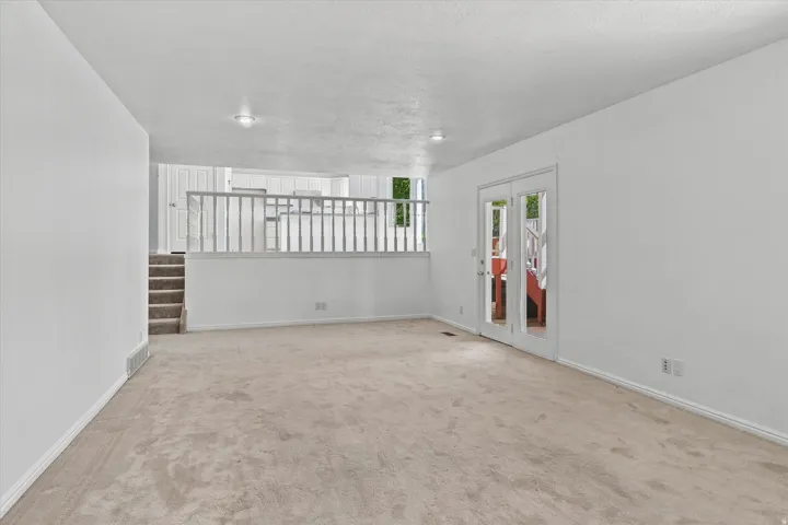 Spacious room featuring neutral carpeting, white walls, recessed lighting, and a double glass-panel door