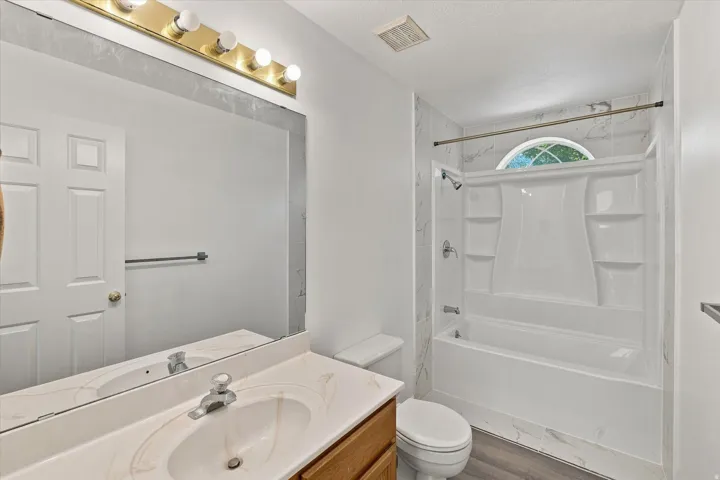 Bathroom featuring a vanity with an integrated sink, a full-width mirror, overhead lighting, a toilet, and a combined tub and shower unit with a window