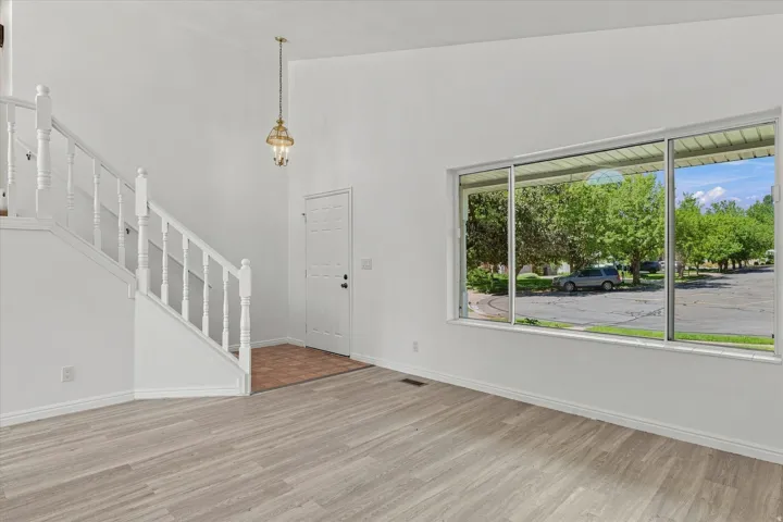 Wood-finish flooring, white painted staircase with balusters, high ceilings, large multi-pane window, and a decorative pendant light fixture