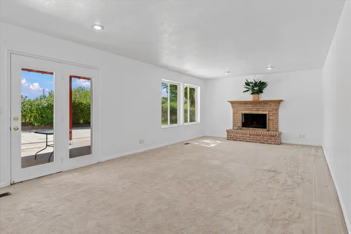 Spacious room with light-colored carpeting, a brick fireplace, and a wood mantel