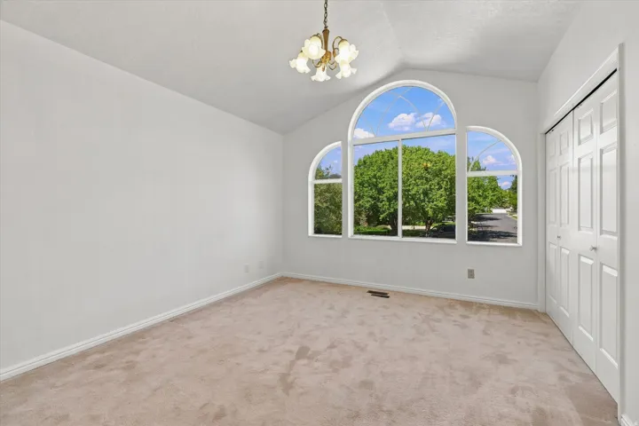 Vaulted ceiling with an attached chandelier, arch-top windows, and carpet flooring