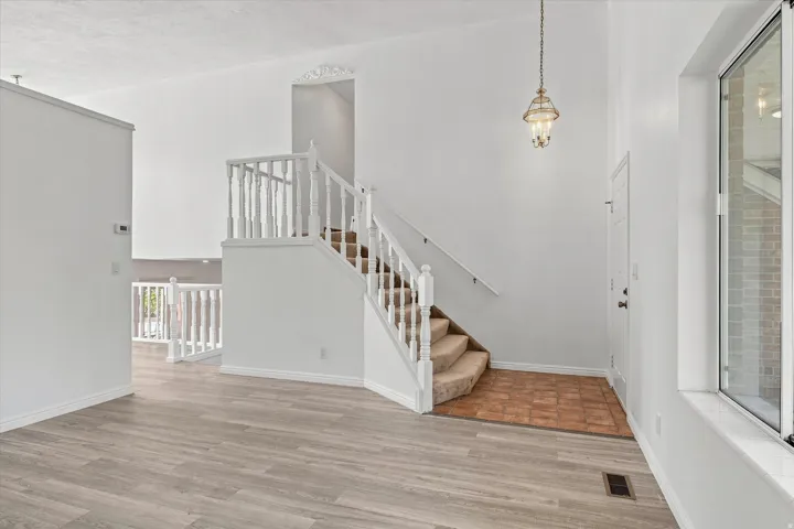 Wood-finish flooring, staircase with carpeted treads and white balusters, decorative ceiling light fixture, high ceilings, and a large window with white trim