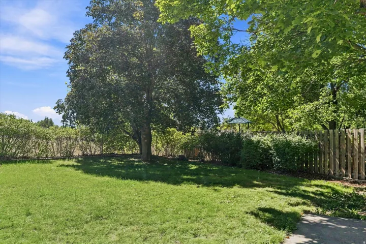 Expansive green lawn with mature trees, established shrubs, and wood fencing