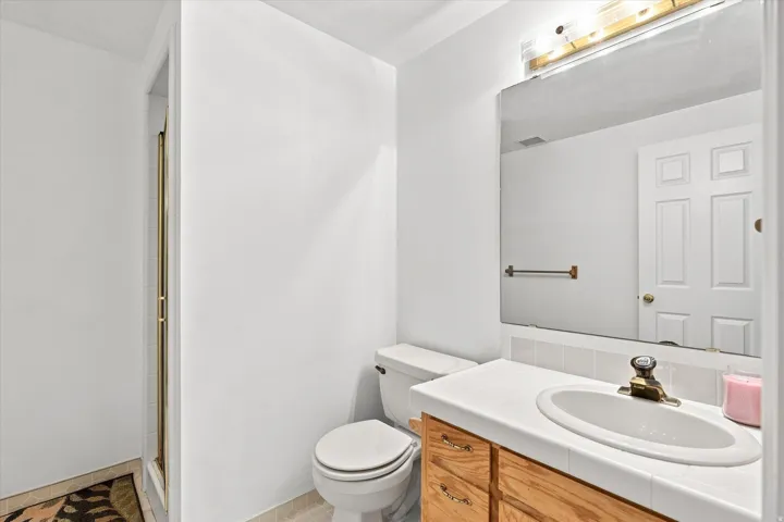 White tile countertop with an integrated oval sink, wood-finish vanity cabinetry, and a large wall-mounted mirror