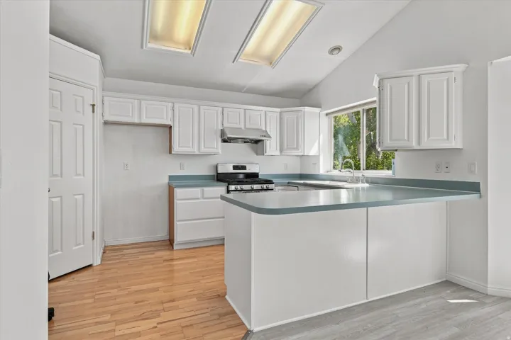 Kitchen featuring vaulted ceilings, white cabinetry, light-colored wood-finish flooring, a stainless steel range, and a breakfast bar