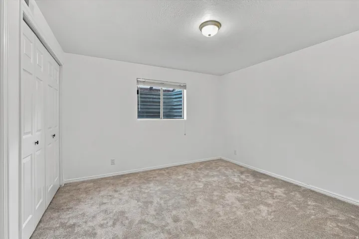 Neutral-toned carpeting, white walls, and a window with blinds