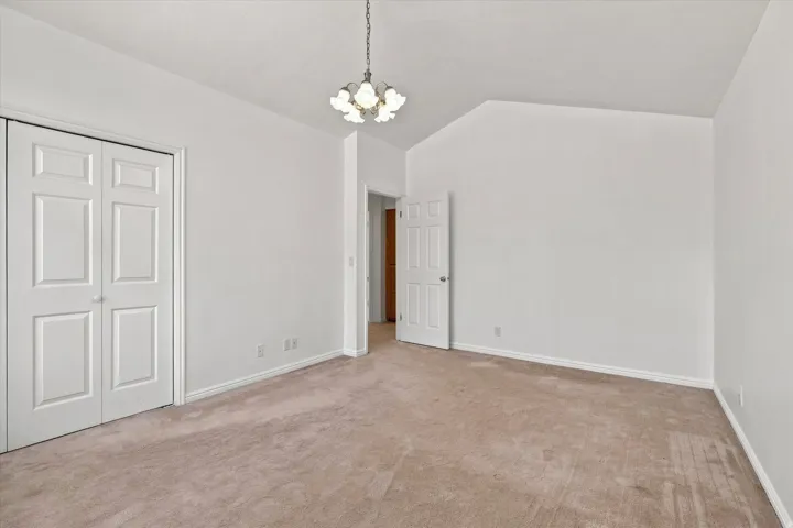 Vaulted ceiling with an attached chandelier, neutral wall paint, and plush carpeting