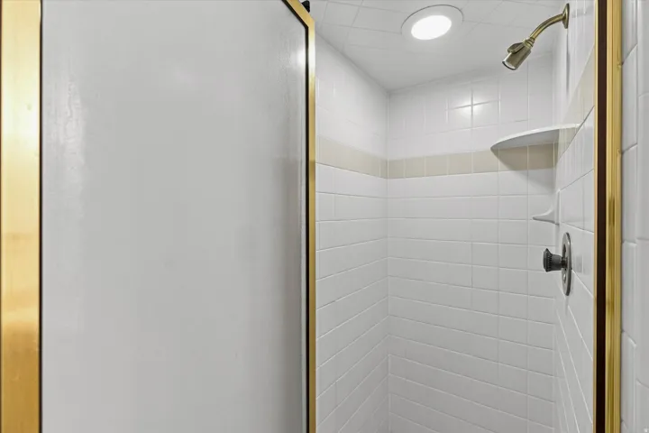 Tiled shower enclosure featuring a recessed light, built-in shelving, and a brass-tone shower head