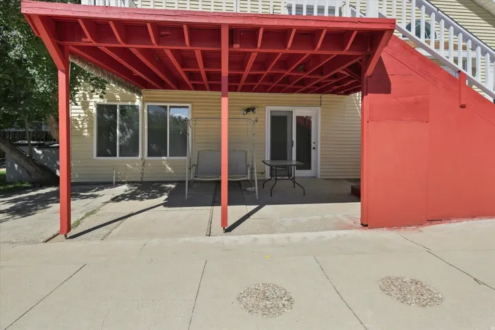 Patio area featuring a red wooden awning, light-colored siding, multiple windows, and a sliding glass door