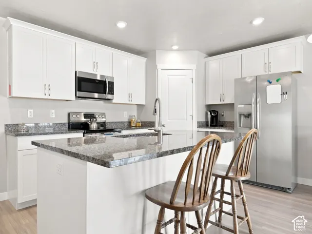 White cabinetry, stainless steel appliances, recessed lighting, wood-finish flooring, and a kitchen island with stone countertops