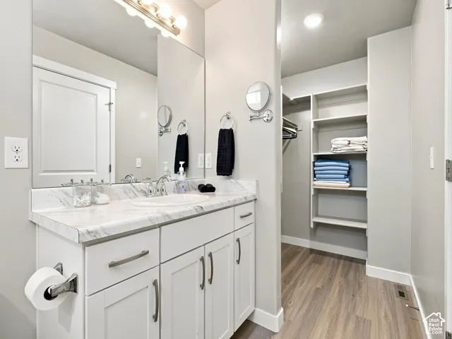 Vanity with a white countertop and integrated sink, white cabinetry with brushed nickel hardware, and wood-finish flooring
