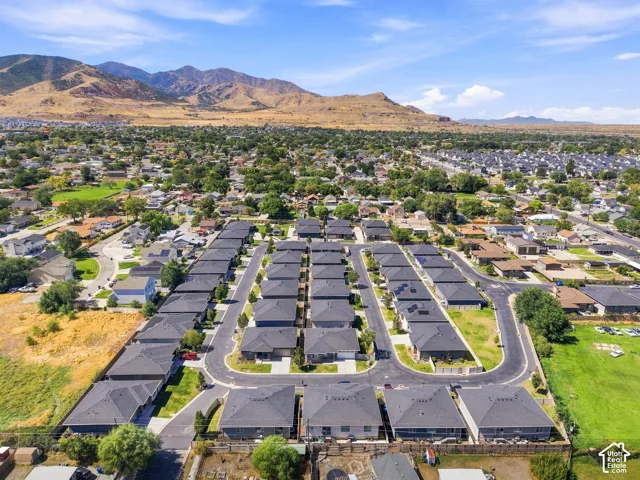 Aerial perspective showcasing a community of properties with dark gray shingle roofs, paved streets, and surrounding green spaces