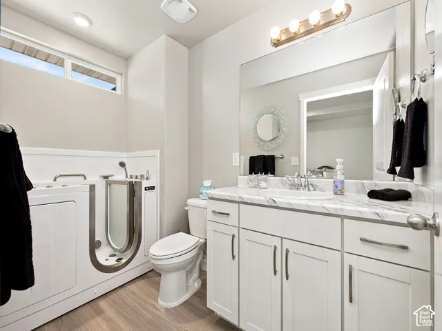Walk-in bathtub, dual-flush toilet, single vanity with undermount sink, marble-finish countertop, and white shaker-style cabinetry