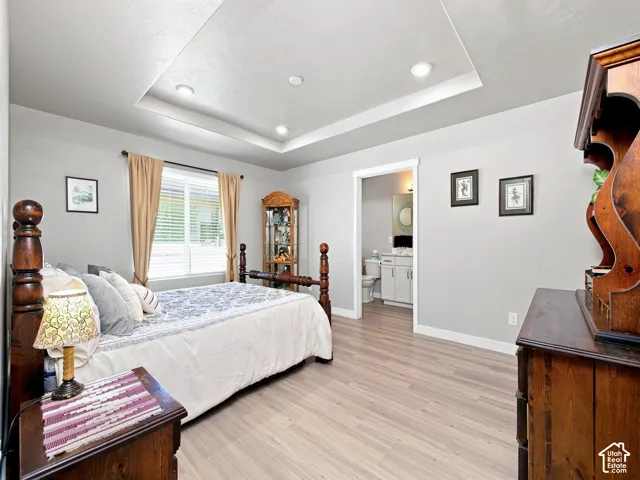 Tray ceiling with recessed lighting, wood-finish flooring, white trim, and direct access to a bathroom with a vanity