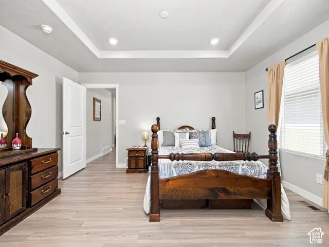 Tray ceiling with recessed lighting, light wood-finish flooring, white door, and window with blinds