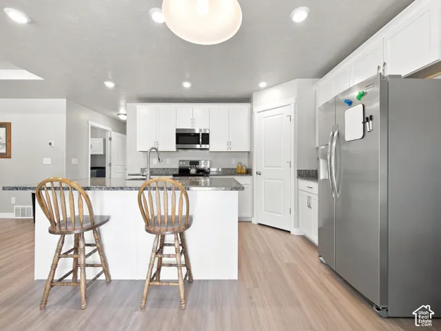 Bright kitchen with white cabinetry, stainless steel appliances, a center island with countertop seating, and wood-finish flooring