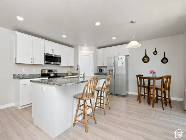 Kitchen featuring white cabinetry, stainless steel appliances, granite countertops, and wood-finish flooring