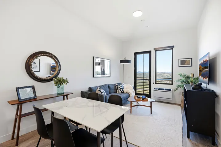 Open-concept living area featuring high ceilings, wood-finish flooring, a contemporary dining table with a white top, and floor-to-ceiling windows