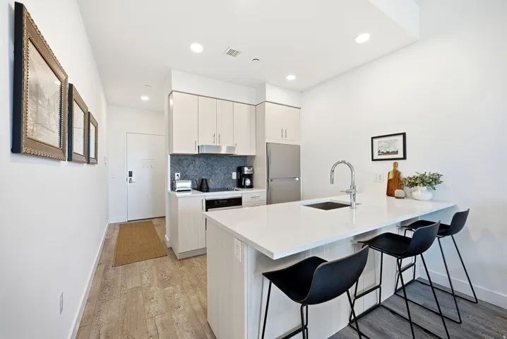 Contemporary kitchen featuring light wood-finish cabinetry, stainless steel appliances, a white solid surface island with an integrated sink and gooseneck faucet, and a grey mosaic tile backsplash