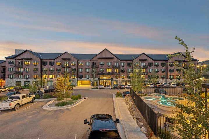 Multi-story building featuring stone and wood-finish siding, multiple balconies, a structured parking area, and a tiered pool with integrated lighting