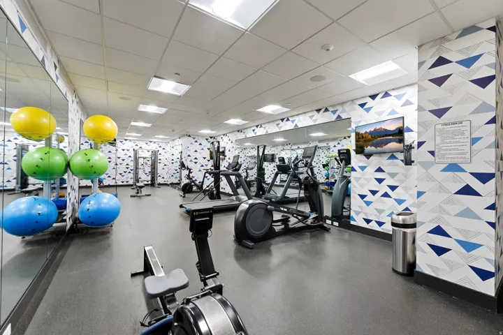 Fitness facility with resilient flooring, mirrored wall, recessed lighting, and wall-mounted television