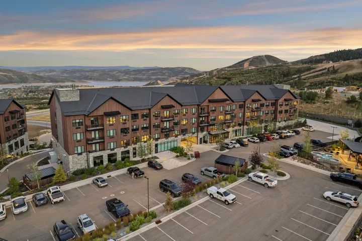 Multi-story building featuring stone and wood-panel exterior, private balconies, and an expansive parking area