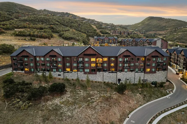 Multi-level building with dark wood siding, stone foundation, dark shingle roof, and multiple balconies