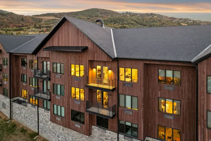 Multi-story building featuring wood-finish siding, stone-finish foundation, multiple balconies with metal railings, and a dark shingle roof