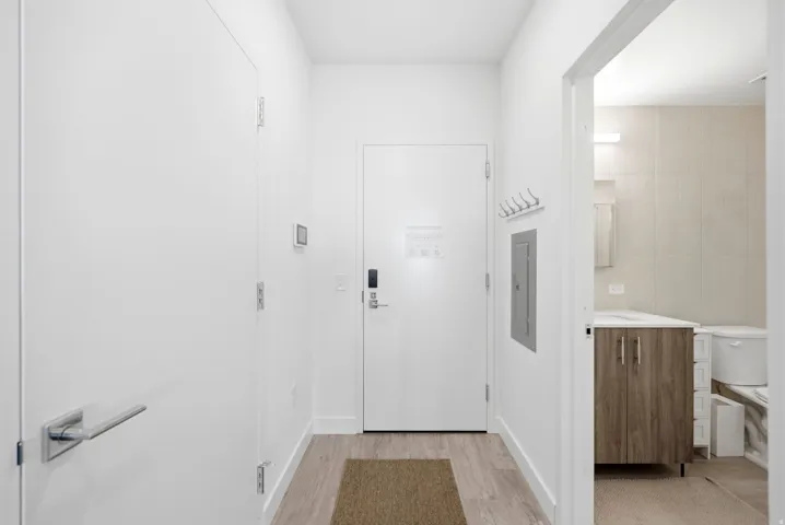 Wood-finish flooring with a white door, sleek hardware, and an adjacent bathroom featuring a wood-finish vanity
