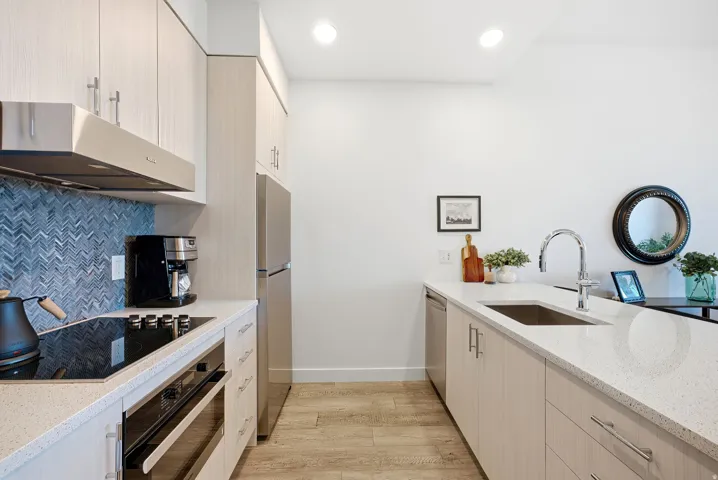 Kitchen featuring light wood-finish cabinetry, stainless steel appliances, a chevron pattern tile backsplash, and light-toned countertops