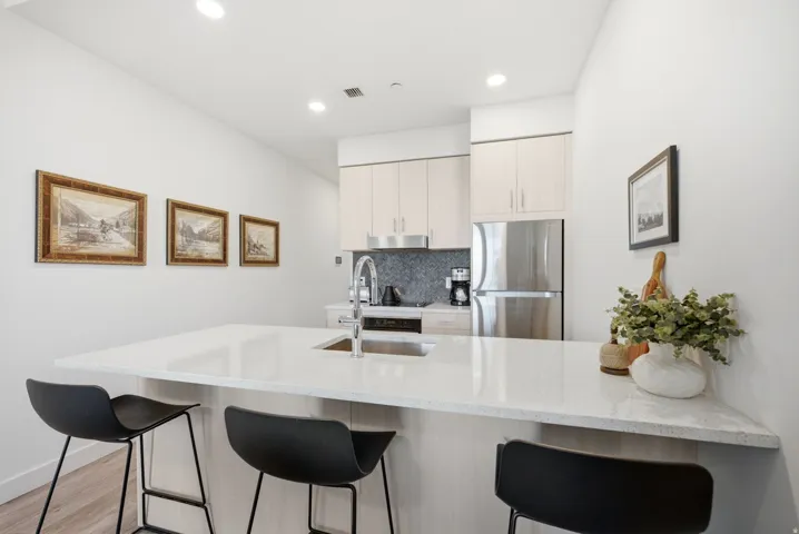 Kitchen featuring a large island with an undermount sink, light wood-finish cabinetry, stainless steel appliances, and a dark tile backsplash