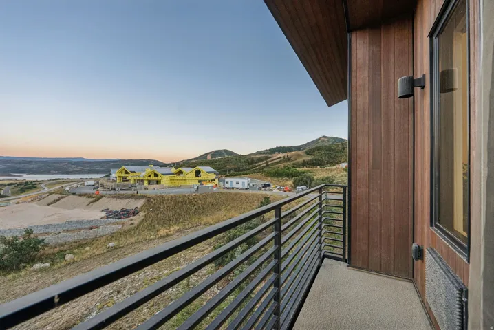 Balcony with metal railings, featuring wood-look siding, a wall-mounted light fixture, and a window with dark trim