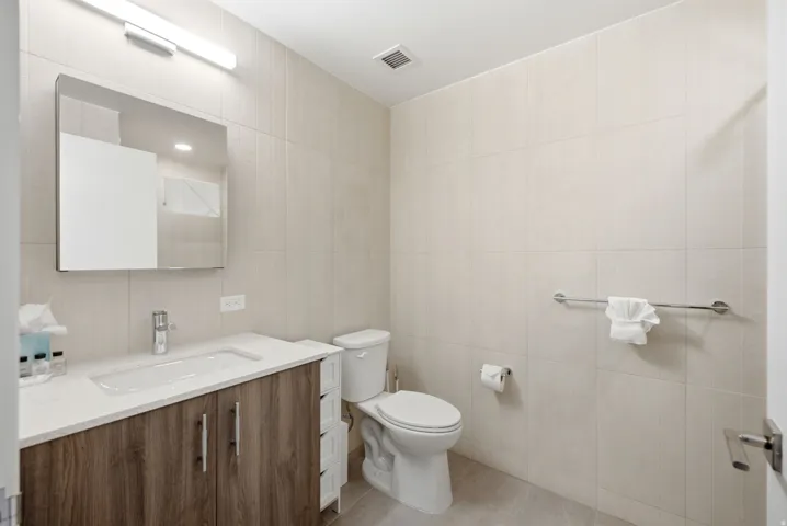 Bathroom featuring a wood-finish vanity with a white countertop, an integrated rectangular sink, a chrome faucet, and tiled walls