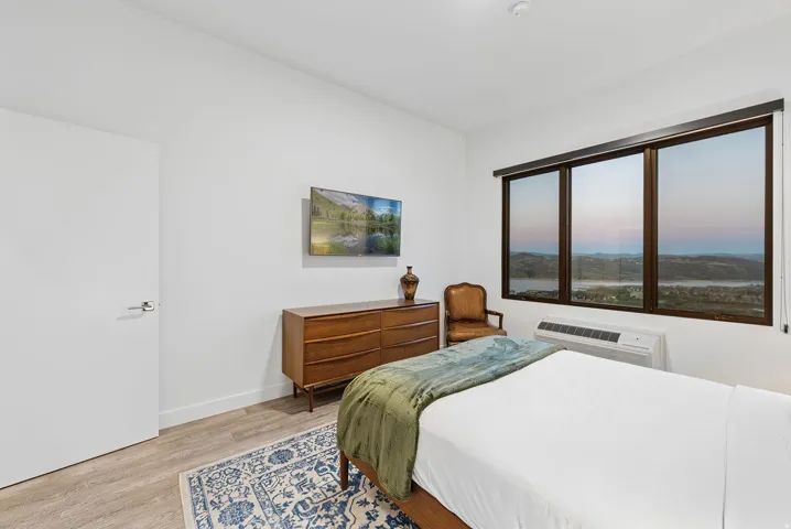 Wall-mounted television, large window with expansive scenery, wood-finish flooring, and white walls