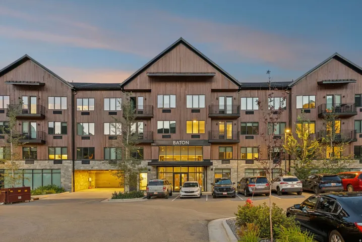 Building exterior featuring wood-finish siding, stone accents, multiple balconies, a covered entry, and dedicated surface parking