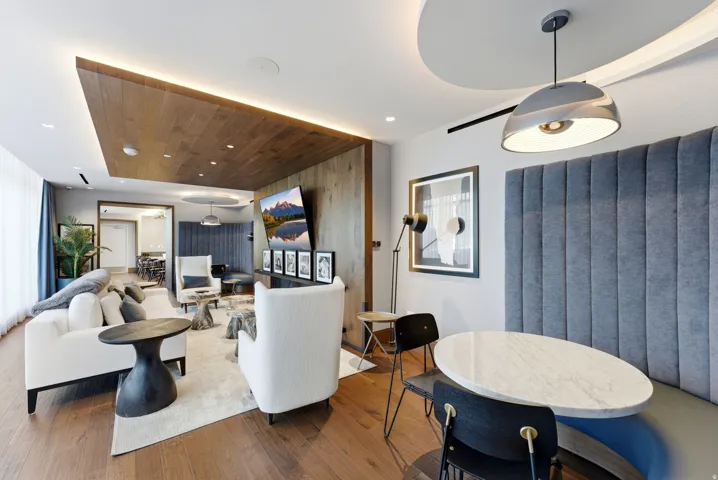 Wood-finish flooring, recessed lighting, wood-paneled ceiling accent with perimeter lighting, curved banquette seating with vertical channel tufting, and a circular marble-look table