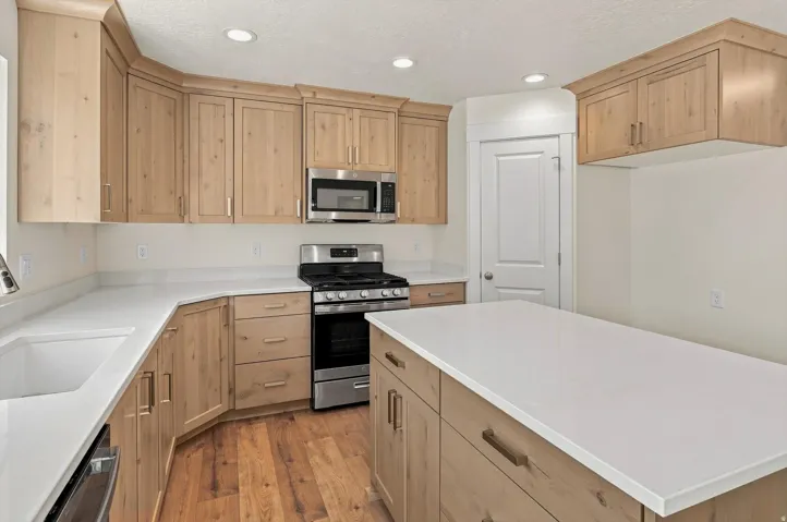 Kitchen featuring wood-finish cabinetry, stainless steel appliances, white countertops, a kitchen island, and wood-finish flooring