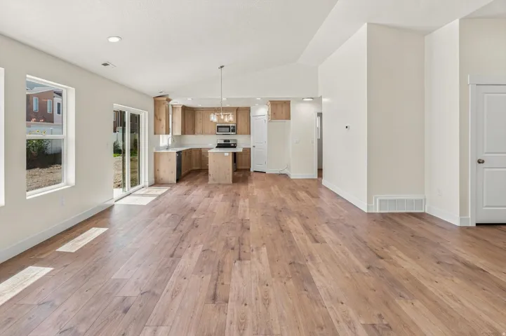 Open-concept living area with wood-finish flooring, vaulted ceilings, recessed lighting, and a modern kitchen featuring light wood cabinetry, a center island, and stainless steel appliances