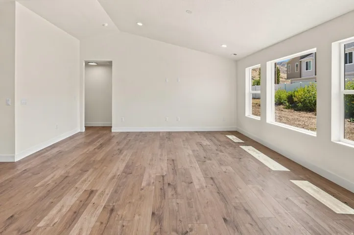 Wood-finish flooring, recessed lighting, white walls, multiple windows, and vaulted ceilings