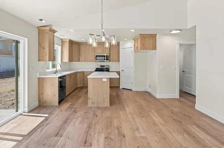 Light wood-finish flooring, vaulted ceilings, and a kitchen island with a white countertop