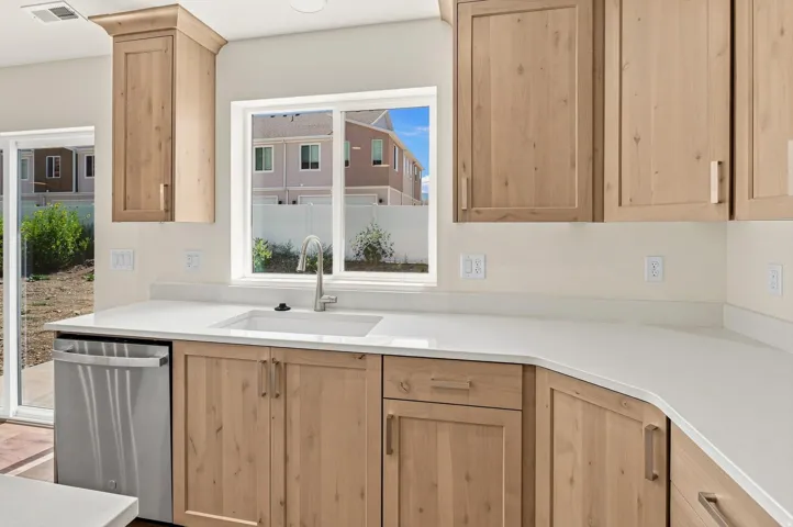 Contemporary kitchen featuring light wood cabinetry, white countertops, a stainless steel sink with a gooseneck faucet, a stainless steel dishwasher, and a sliding glass door