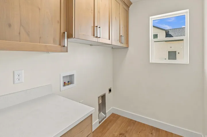 Light wood-finish cabinetry, white solid surface countertop, wood-finish flooring, and a window providing natural illumination